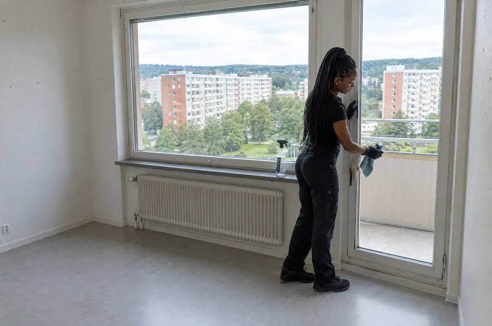 Flyttstädning av en hyreslägenhet i Angered: städare i svart torkar fönsterkarm och balkongdörr
