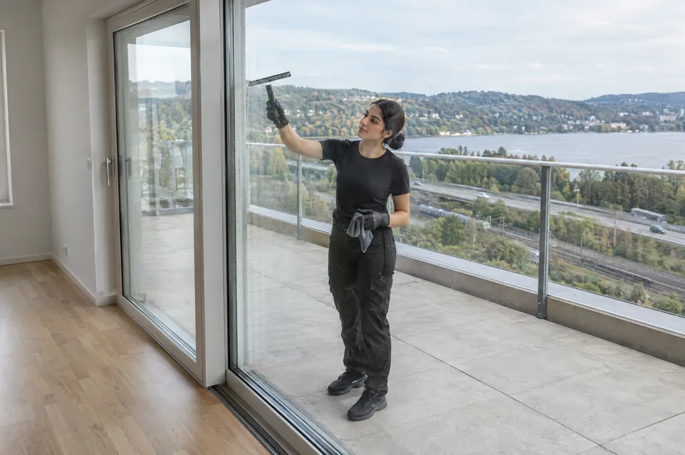 Flyttstädning av en terrasslägenhet i Bohus: städare i svart putsar glasdörren mot terrassen